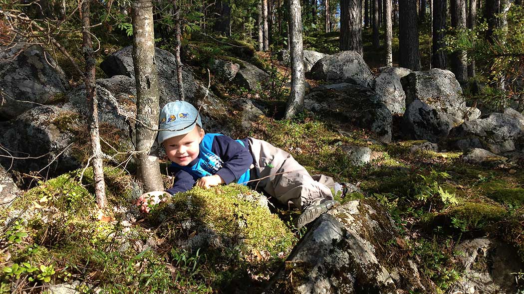 Ett leende barn ligger på en mossig sten i skogen.