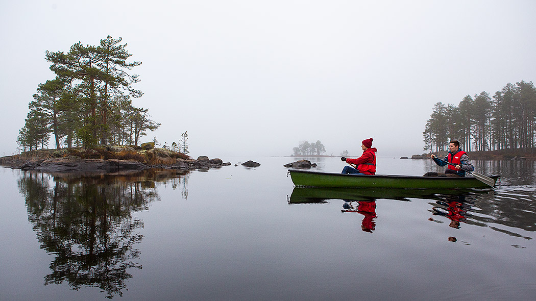 Folk paddlar kanot på en dimmig sjö.