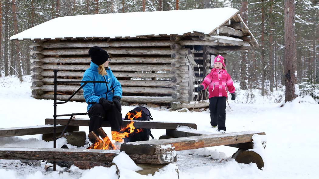En vuxen och ett barn tillbringar tid runt en lägereld i en snöig skog.