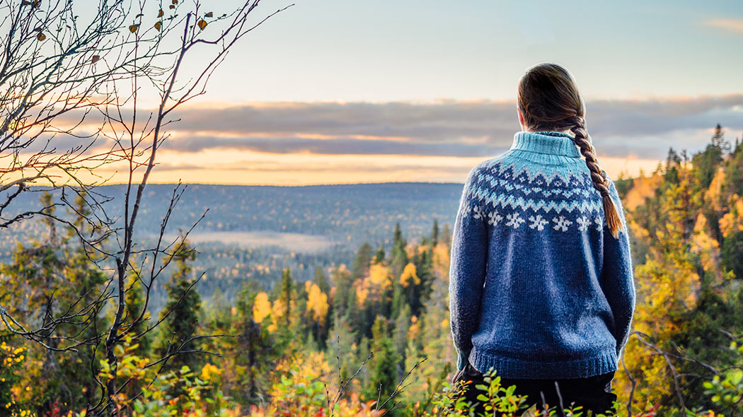 En vandrare iklädd en tröja står vid hösten och det färgstarka landskapet som öppnar sig från faran på baksidan av fotografen.
