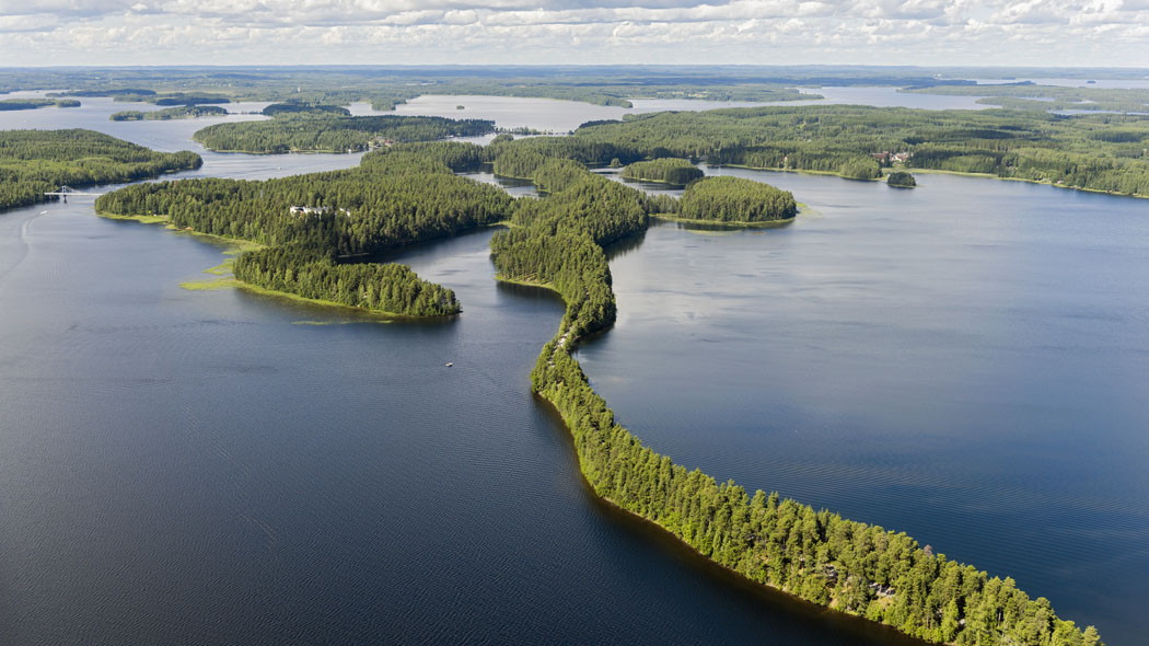 Ett flygfotografi av ett sjölandskap som sträcker sig till horisonten. I landskapet finns skog och sjöar om vartannat. På bilden kan även en lång och smal ås ses.