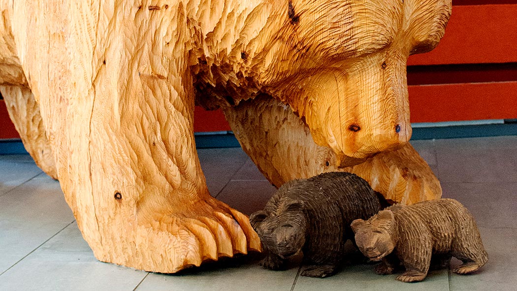 Tre björnar gjorda i trä inomhus på golvet, en är stor och två är små.