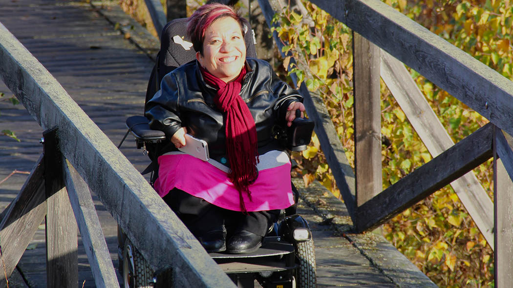 En person i rullstol kör längs en träramp i soligt höstväder.